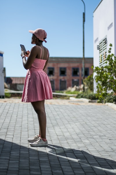 穿着粉红色细肩带迷你连衣裙的女人使用智能手机
